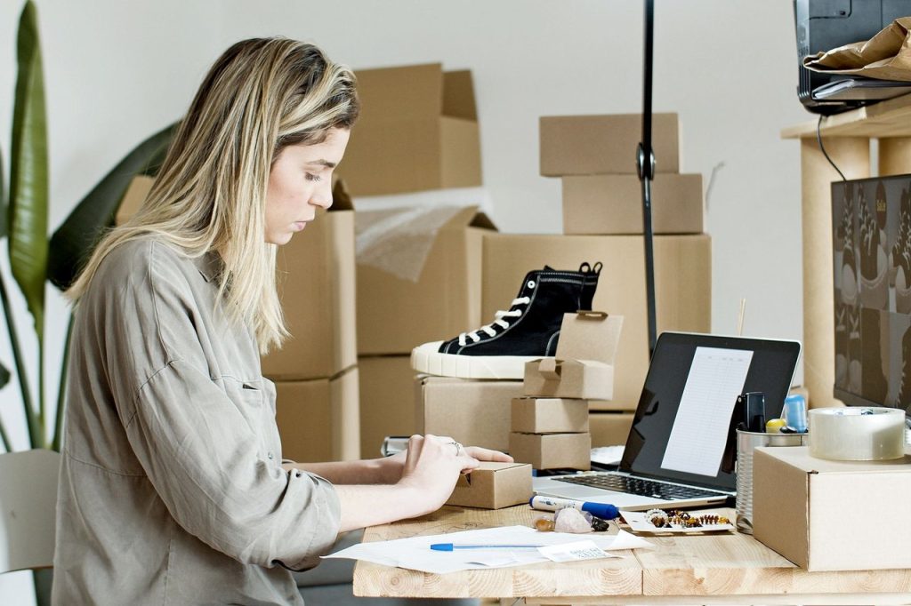 Medidas para microempreendedores incluem proposta de perdão de dívidas e mais crédito Mulher embala caixas em uma loja on-line, cercada por materiais de embalagem e um computador portátil.