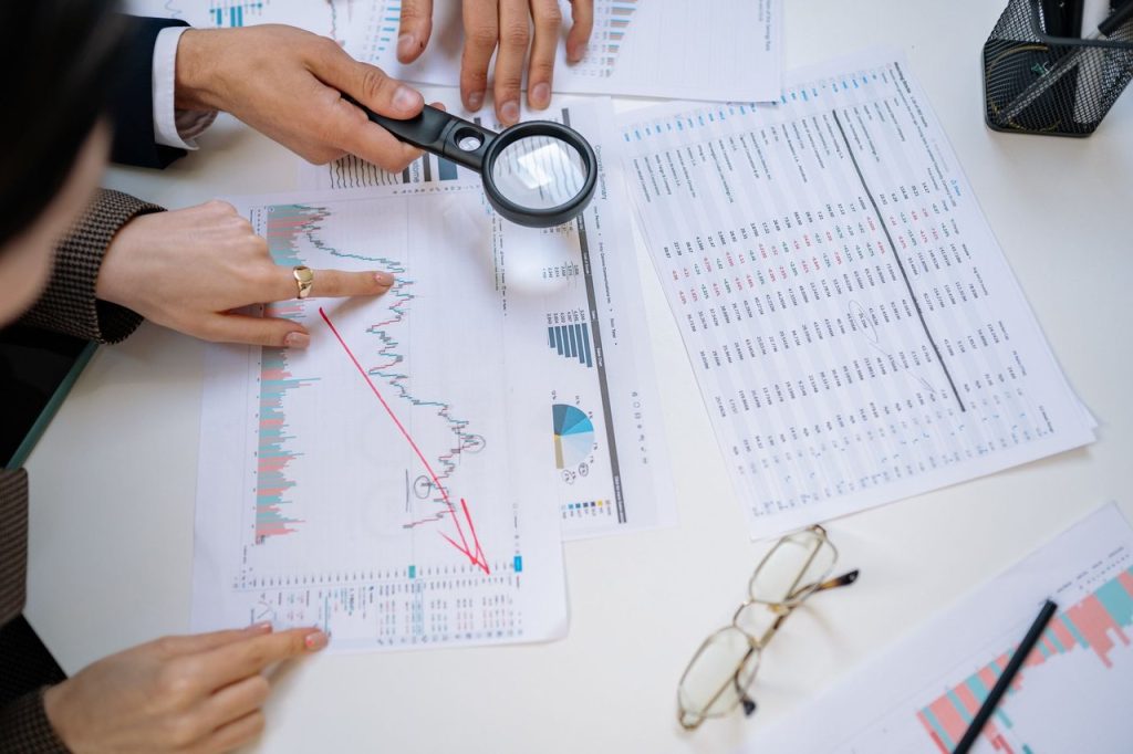 Profissionais analisam documentos financeiros com uma lupa em um ambiente de escritório.