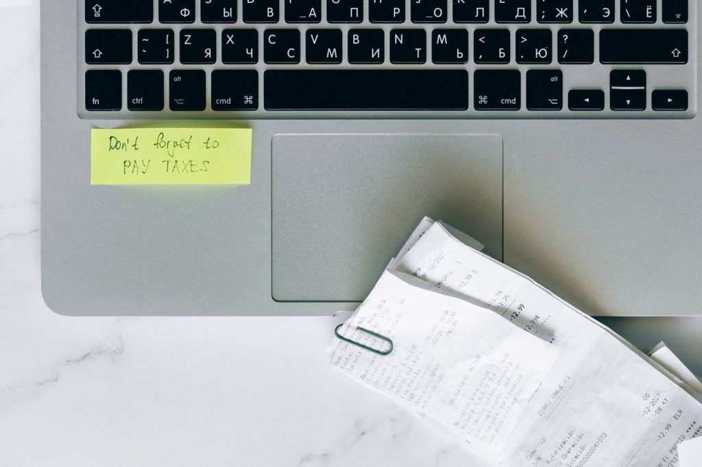 Restituição residual do IR será depositada a 184 mil contribuintes em outubro Laptop ao lado de recibos e um lembrete adesivo sobre uma mesa, representando a organização para consulta financeira.