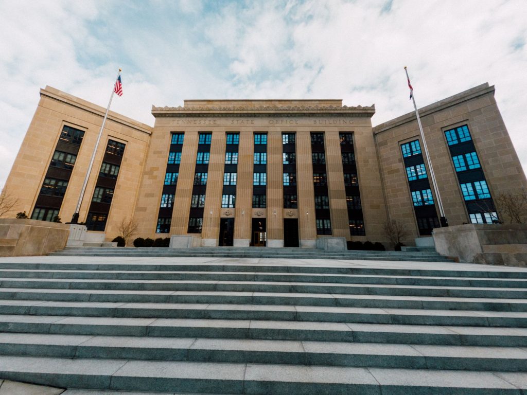 Exterior do edifício do Federal Reserve nos Estados Unidos, visto de baixo, com bandeiras americanas e céu nublado.
