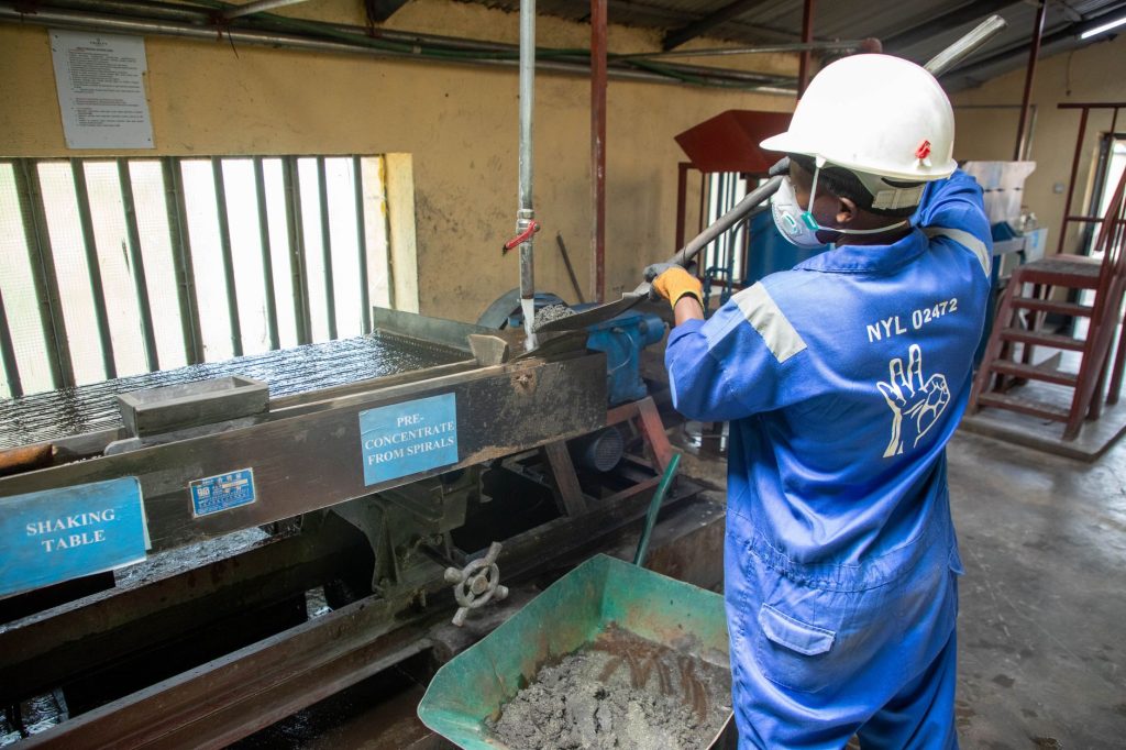Trabalhador usando equipamento de mesa vibratória para processar minério em uma unidade industrial.